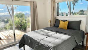 Ein Schlafzimmer mit einem großen Bett, einem Deckenventilator und Blick auf einen Garten und Berge.