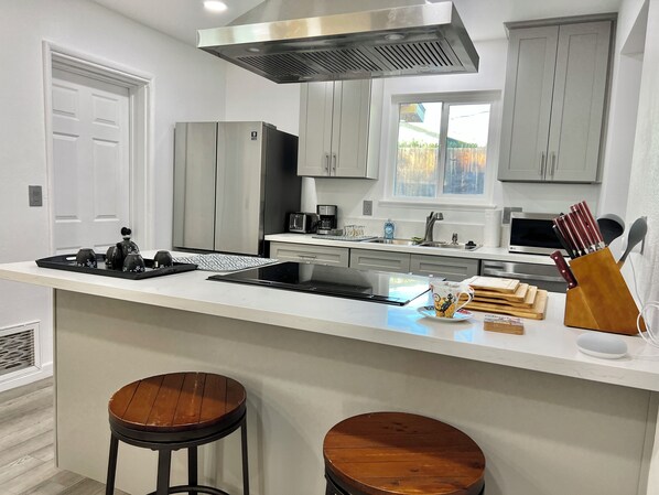 Una cocina moderna con armarios grises, una campana extractora de acero inoxidable, horno empotrado, microondas y una isla grande con taburetes.