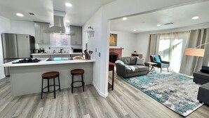 Eine moderne Küche mit einer zentralen Kochinsel, Barhocker und einem Essbereich mit einer Couch und Sesseln.