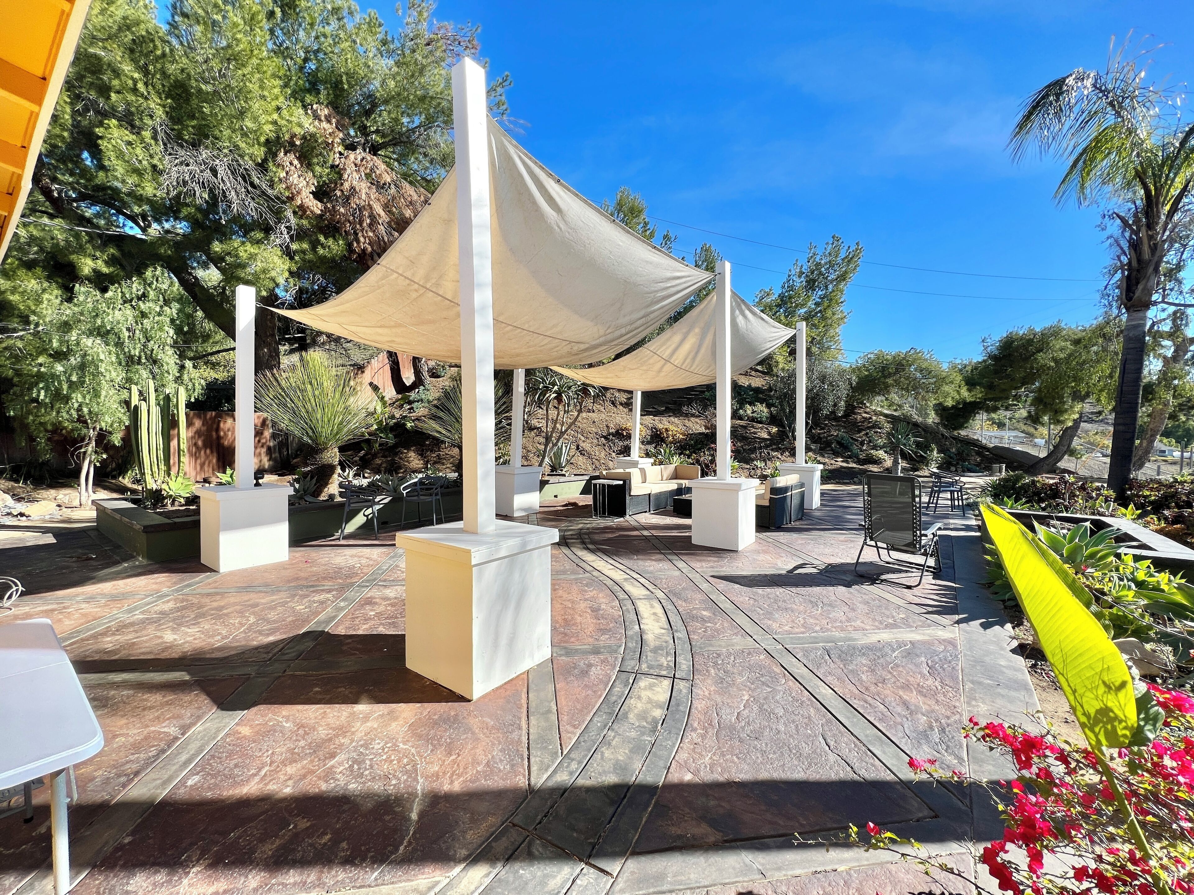 Ein Außenbereich mit Terrasse, Sonnensegel, Sitzgelegenheiten und Pflanzgefäßen.
