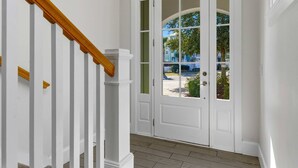 En vit dörr med glaspaneler, en trätrappa med vita räcken och utsikt över en bostadsgata.