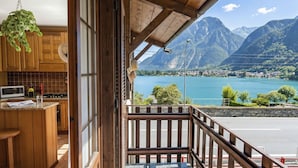 Un balcon en bois offrant une vue sur un lac et des montagnes, une cuisine avec des meubles en bois et une plante suspendue.