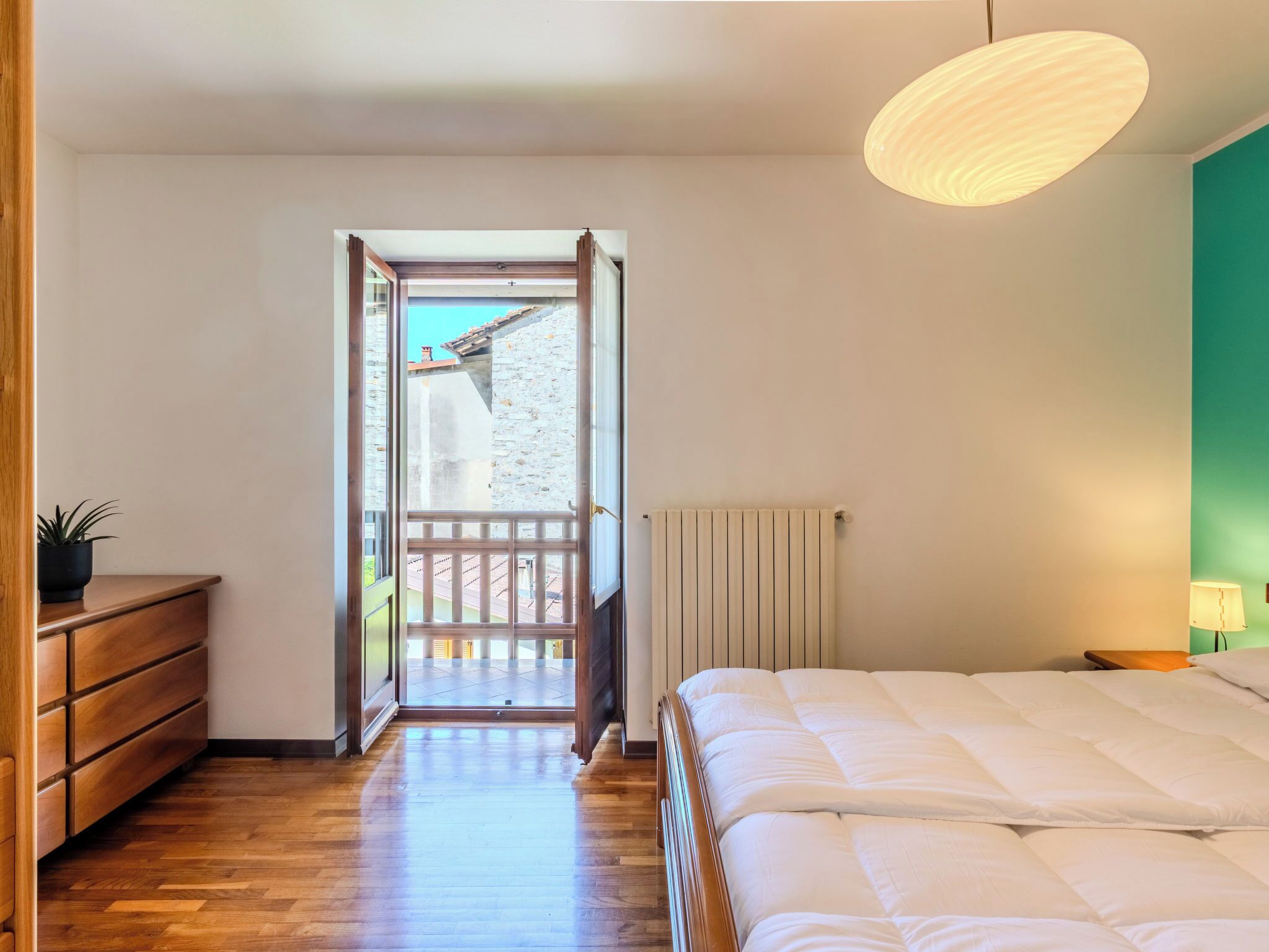 A bedroom with a bed, a dresser, a radiator, and a view of the outside.