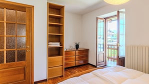 Une chambre à coucher avec un lit, une armoire en bois, une commode et une vue sur l’extérieur, visible à travers une porte.