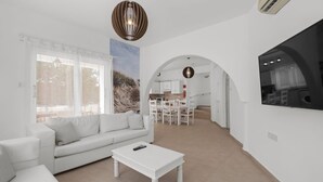 A modern living room with a white sofa, a coffee table, and a dining area with a table and chairs. - Villa Kallidora, 4 BDR, Private Pool, Furnished Terrace, Ayia Napa, Cyprus (Famagusta)