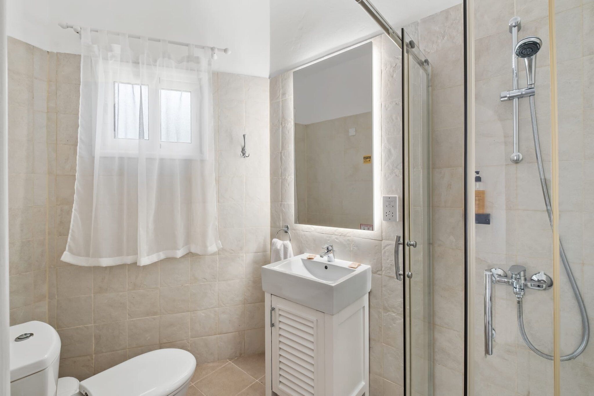 A bathroom with a toilet, sink, shower, and a window with a curtain.