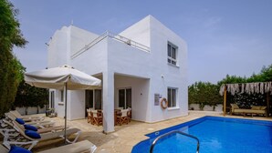 A modern white building with a swimming pool, sun loungers, and outdoor furniture. - Villa Kallidora, 4 BDR, Private Pool, Furnished Terrace, Ayia Napa, Cyprus (Famagusta)