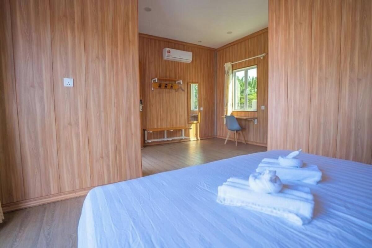 A room with wooden paneling, a bed with neatly folded towels, a bench, a chair, and a window with a view of greenery.