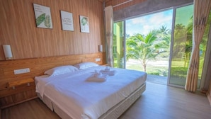 A hotel room with a large bed, wooden walls, and a view of palm trees through a sliding glass door. - Rich Villa  (Semporna)