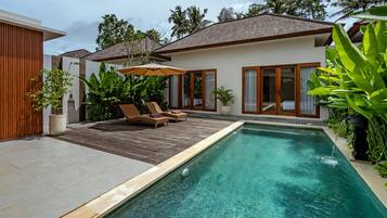 A modern house with a swimming pool, wooden deck, and lounge chairs.
