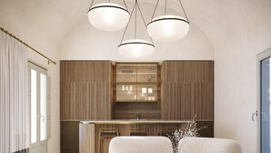 Een moderne woonkamer met een grote L-zitsbank, een ronde salontafel en een keukenhoek met houten keukenkastjes en hanglampen.