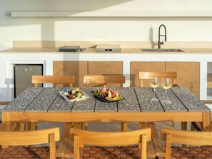 A modern kitchen with a built-in sink, a small refrigerator, and a dining area with a table set for two. - Villa Damaris, Divine Sunset & Sea Views, Private Pool, Furnished Terrace, Oia (Santorini)