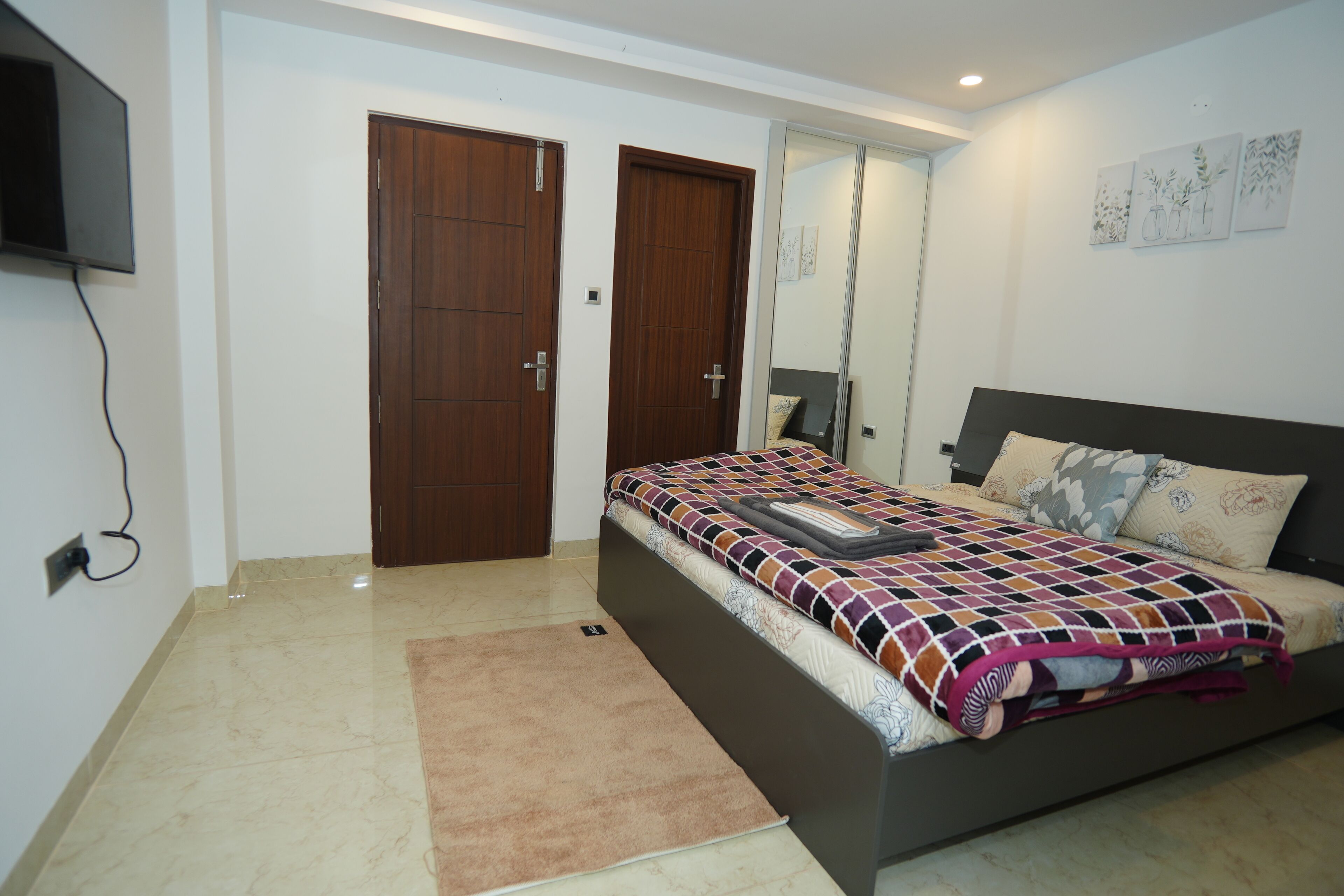 Quarto com cama, televisão fixada na parede e duas portas de madeira.