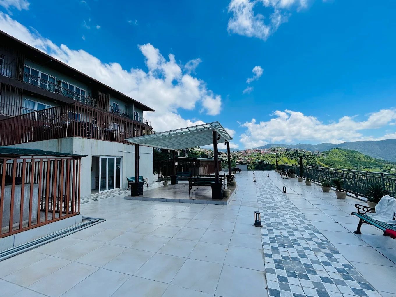 A spacious outdoor terrace with a clear view of the mountains, a covered seating area, and a building with balconies.