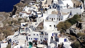 A coastal village with white-washed buildings, steeply pitched roofs, and a narrow street winding through the area. - Thelia Suite, Divine Sunset & Sea Views, Private Jacuzzi, Furnished Terrace, Oia (Santorini)