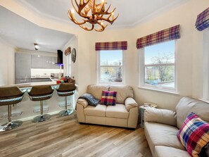 A modern kitchen with a central island, a dining area with bar stools, a sofa, and plaid curtains. - Beautiful modern first floor apartment in Banchory. (Banchory)