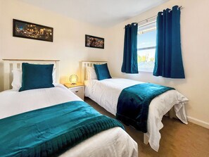 A hotel room with two beds, each with a white and teal bedspread, a nightstand with a lamp, and two framed pictures on the wall.