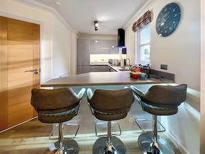 A modern kitchen with a central island, bar stools, and a clock on the wall. - Beautiful modern first floor apartment in Banchory. (Banchory)