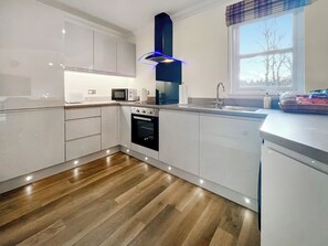 A modern kitchen with white cabinets, a built-in oven, a microwave, and a sink. - Beautiful modern first floor apartment in Banchory. (Banchory)