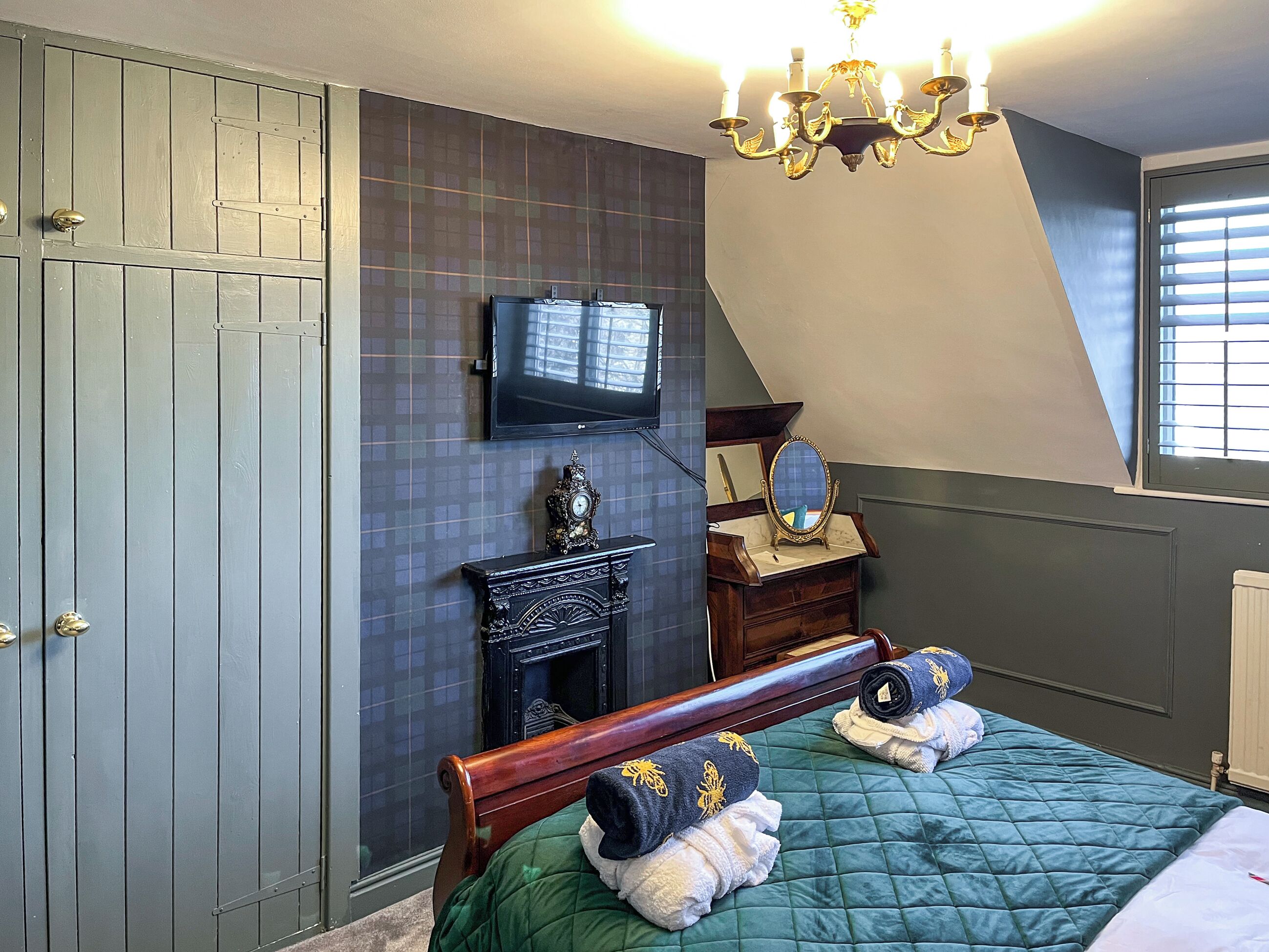 A bedroom with a bed, a dresser, a mirror, a clock, and a television on the wall.