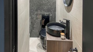 Une salle de bain moderne avec des toilettes noires, un miroir rond et un meuble-lavabo en bois avec un lavabo noir.