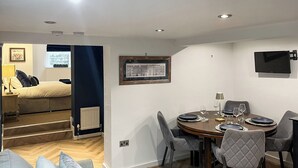 Un espace repas moderne avec une table ronde, des chaises à revêtement gris et un téléviseur à écran plat fixé au mur.