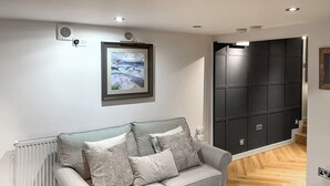 Un salon moderne avec un canapé gris, un tableau encadré, un radiateur et une armoire noire.