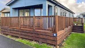 Een laag, blauw gebouw met een houten terras, genummerd 19, met grote ramen en een klein portaaltje.