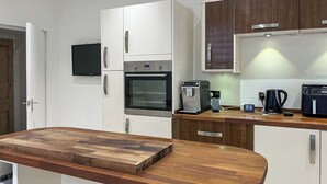 A modern kitchen with white cabinetry, a built-in oven, a coffee machine, and a wooden countertop. - The Quay & Coast Escape (Bridlington)