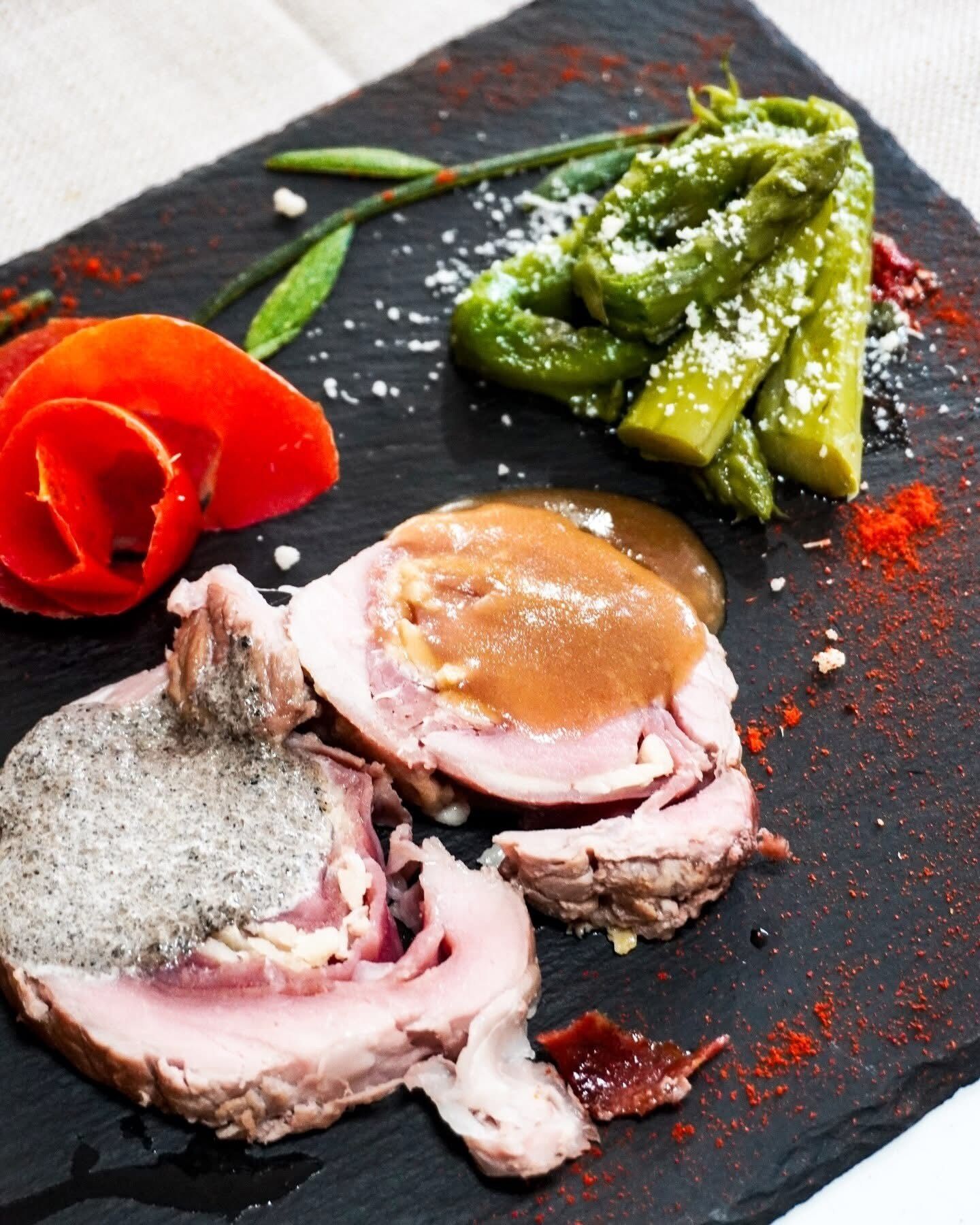 A black slate plate with sliced meat, green asparagus, and a red rose.