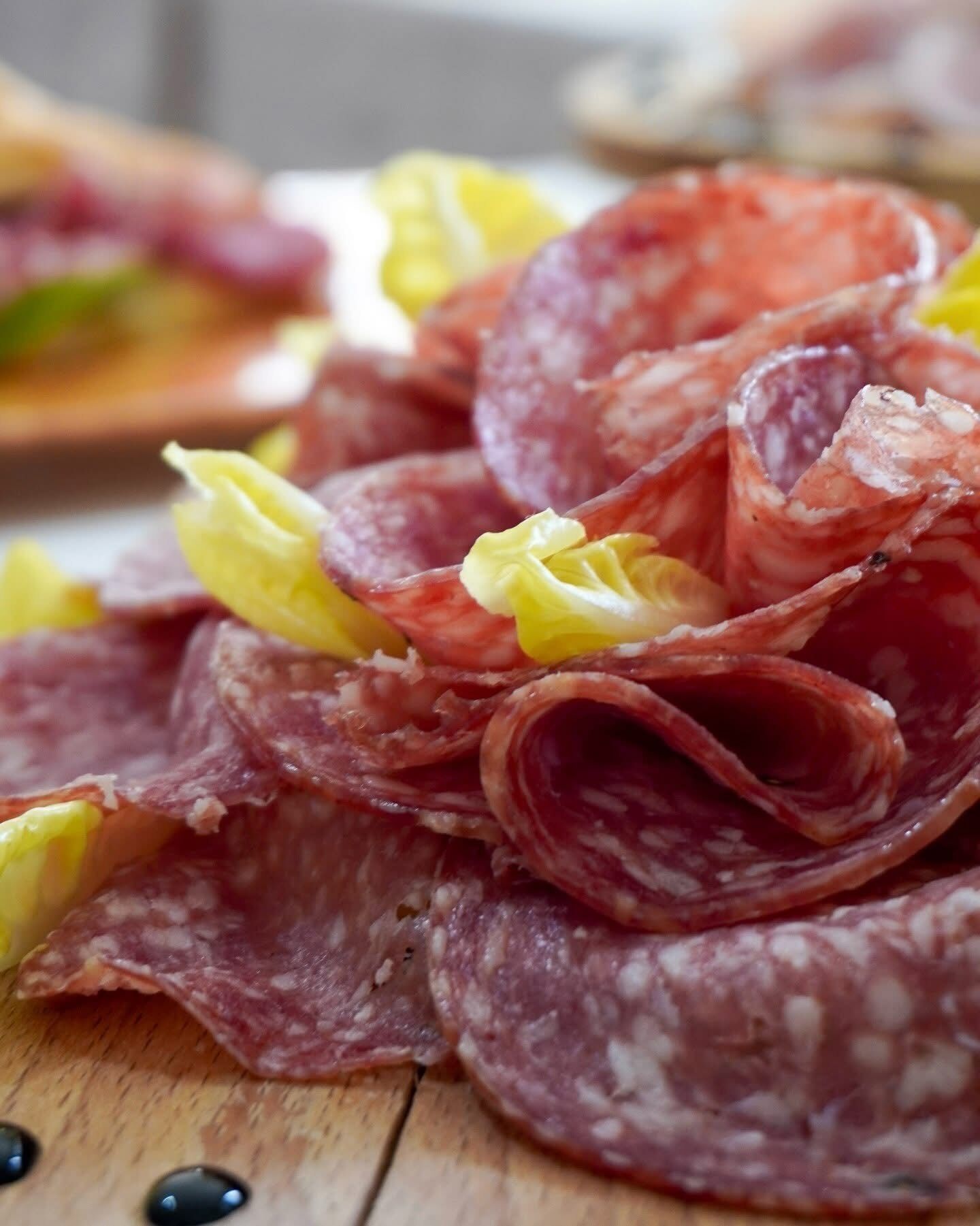A wooden surface with sliced cured meats and yellow flowers.