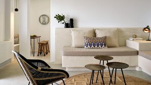 Een moderne woonkamer met een beige bank, een zwarte geweven stoel en drie kleine ronde tafels.