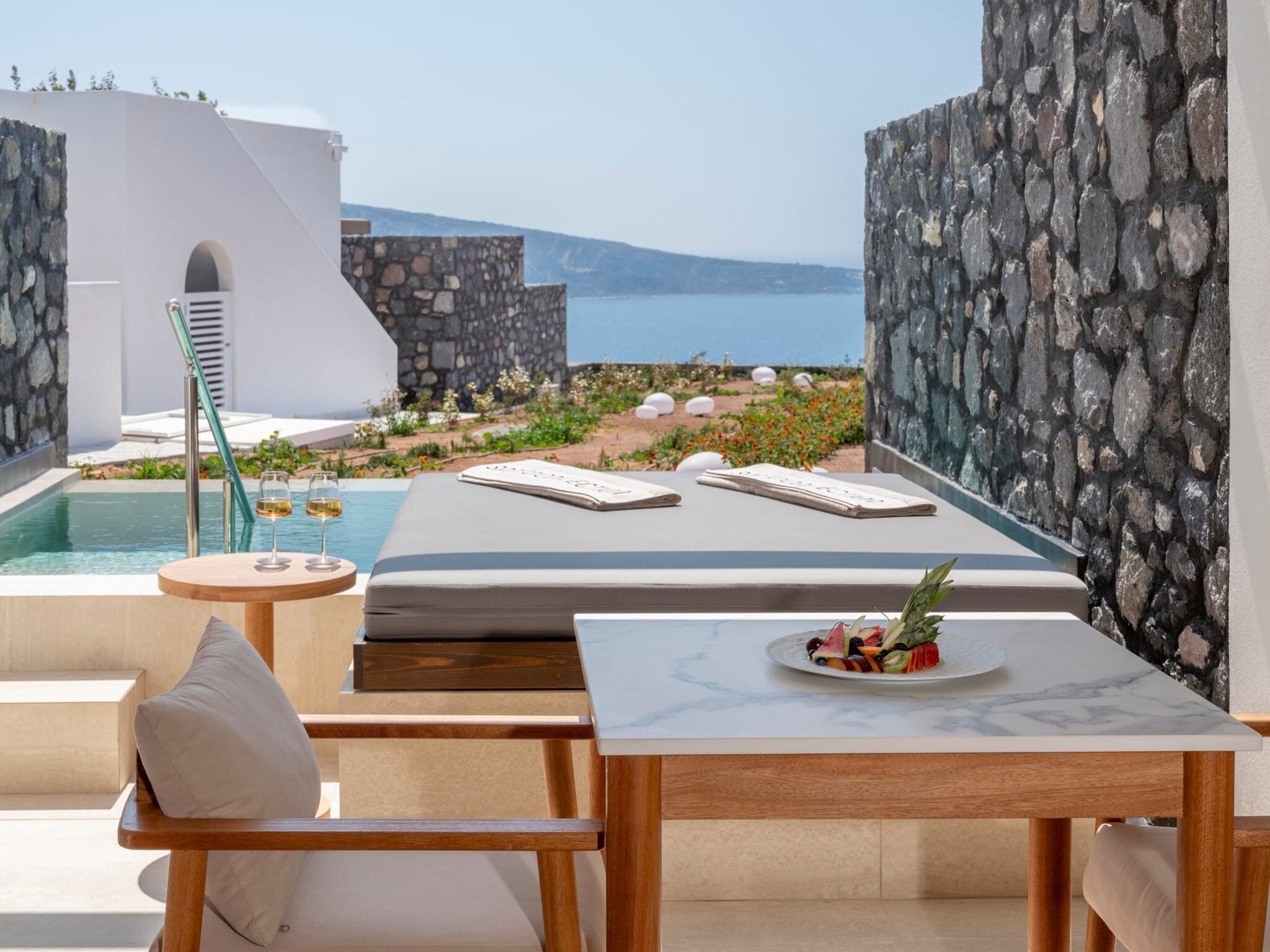 A modern outdoor seating area with a pool, stone walls, and a view of the sea.