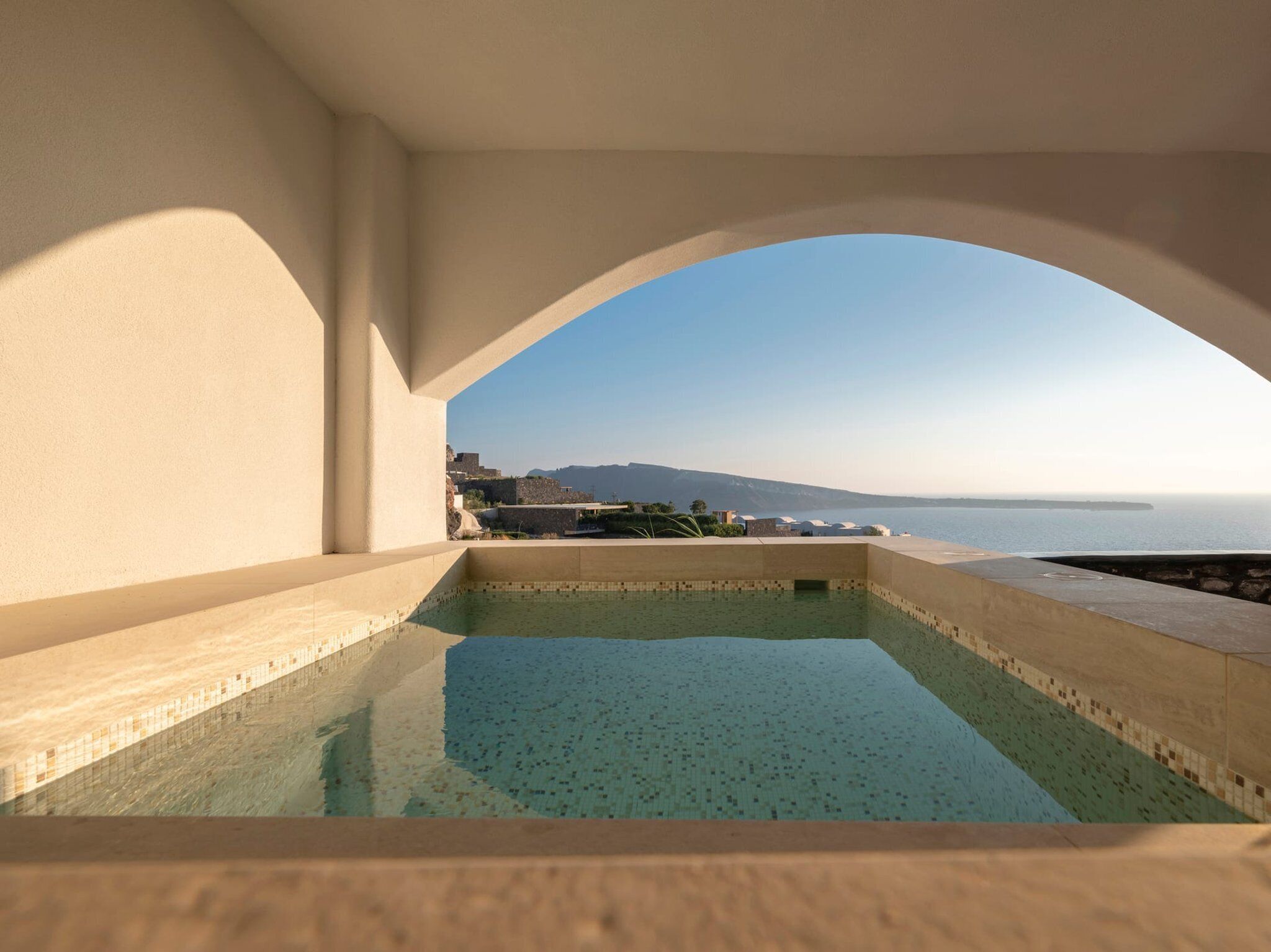 Una piscina a sfioro con vista libera sul mare e colline lontane.