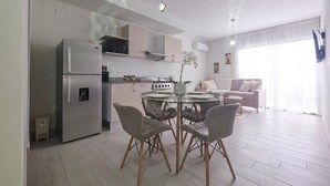 A modern kitchen with a built-in refrigerator, a dining table with chairs, and a living area with a sofa and a TV. - Moderno Apto en B Varo Island Piscina Playa (Punta Cana)