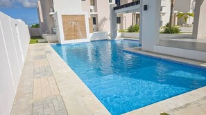 Ein rechteckiger Swimmingpool mit klarem, blauem Wasser, umgeben von einer gefliesten Liegefläche und weißen Wänden.