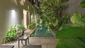 A narrow outdoor pool area with a glass table and chairs, surrounded by lush greenery and potted plants. - Villa Ixora by Alfred in Bali (Canggu)
