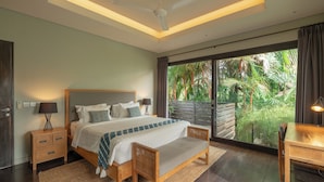 A bedroom with a large bed, bedside tables, a desk, and a view of a lush garden through a sliding glass door. - Villa Ixora by Alfred in Bali (Canggu)