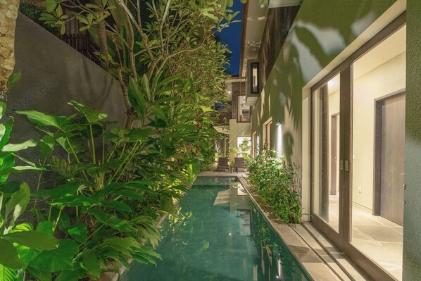 A narrow indoor pool with a tiled floor, surrounded by lush green plants and a modern building with large windows and doors. - Villa Ixora by Alfred in Bali (Canggu)