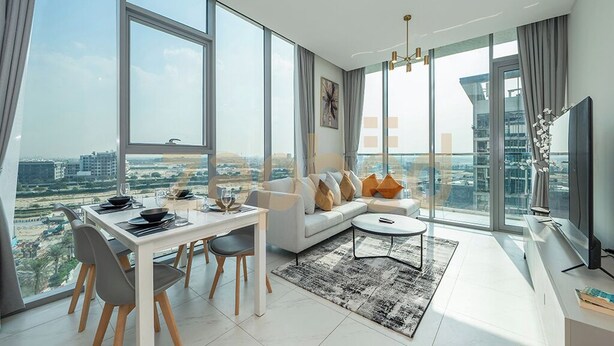 A modern living room with a dining area, large windows, and a city view. - Zapbed-1 BR in District One Residence 16 (Dubai)