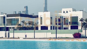 A modern building with a pool in the foreground and a tall skyscraper in the background. - Zapbed-1 BR in District One Residence 16 (Dubai)