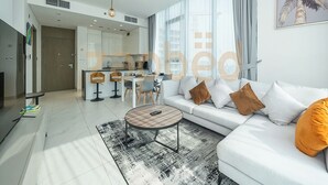 A modern living room with a sofa, coffee table, and a kitchen in the background. - Zapbed-1 BR in District One Residence 16 (Dubai)