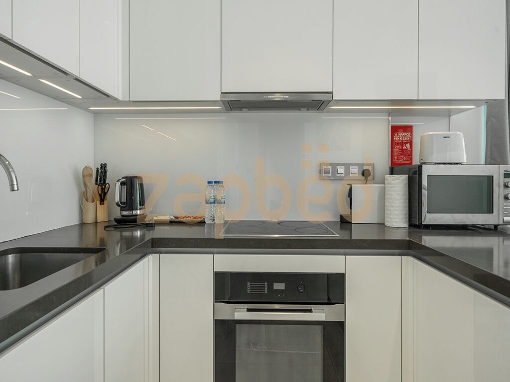A modern kitchen with white cabinets, a stainless steel sink, a built-in dishwasher, a microwave, and a coffee maker.