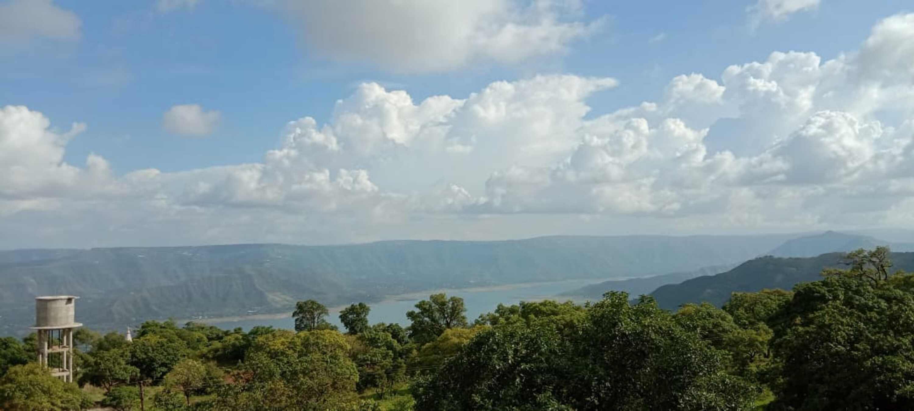 Paisaje montañoso con un cuerpo de agua, árboles y una estructura en primer plano.