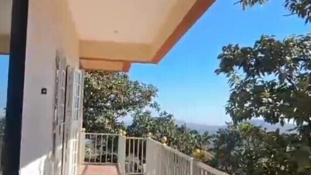 Ein überdachter Balkon mit Geländer, freie Aussicht auf Bäume und eine entfernte Landschaft.