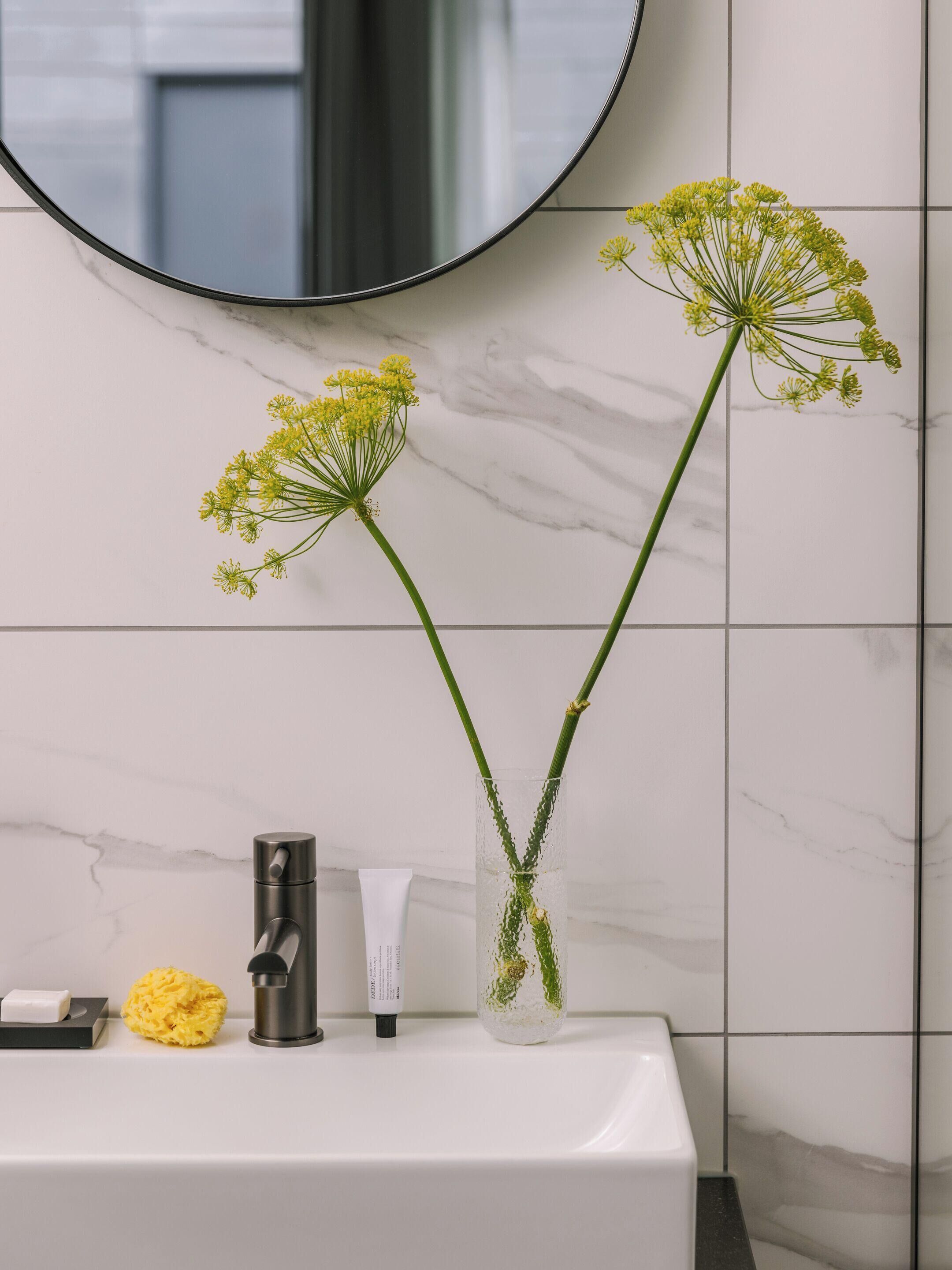 A bathroom with a white sink, a mirror, and two vases with flowers.