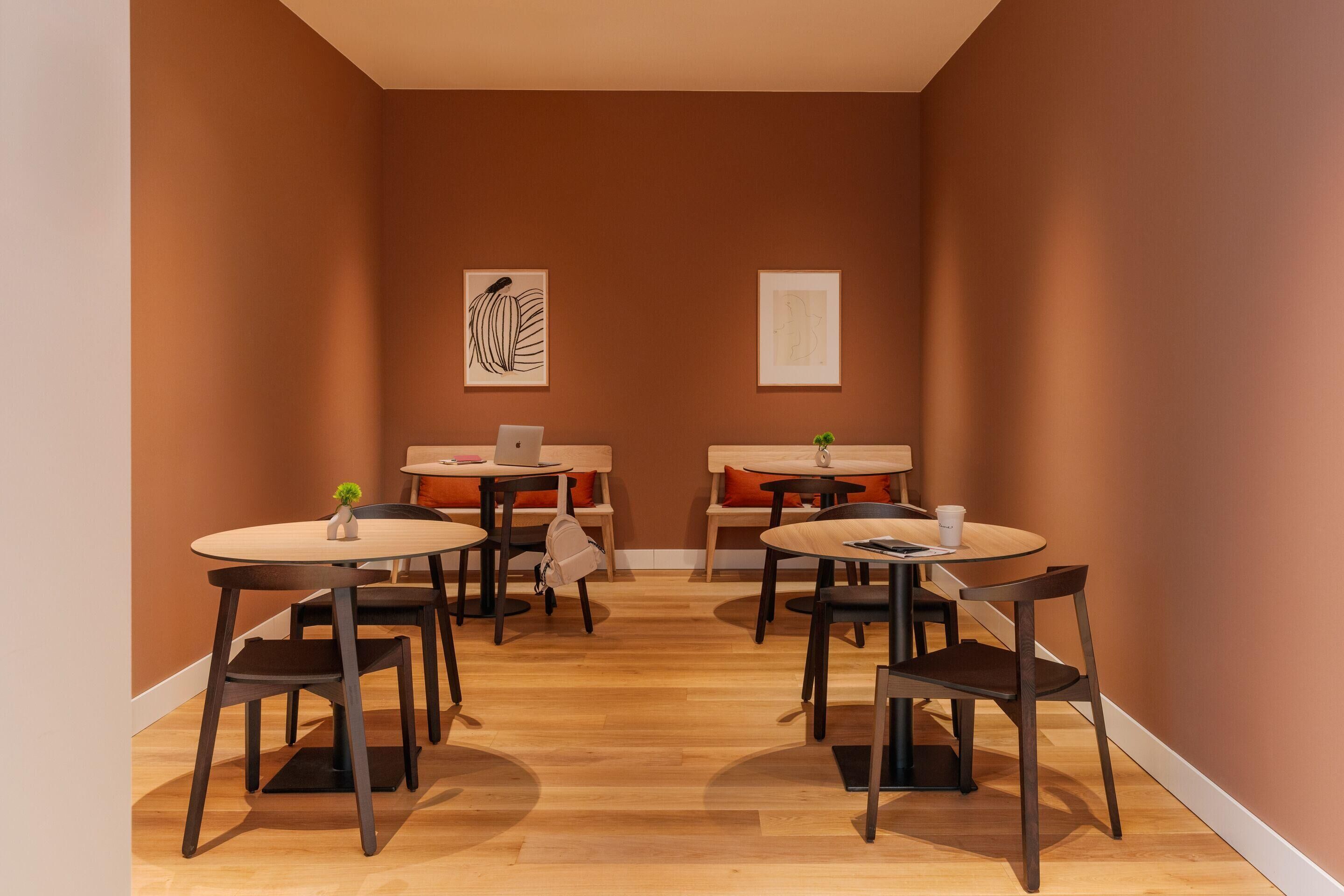 A cozy dining area with round tables and chairs, a laptop on one table, and artwork on the walls.