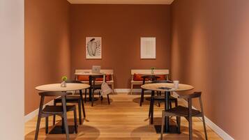 A cozy dining area with round tables and chairs, a laptop on one table, and artwork on the walls.
