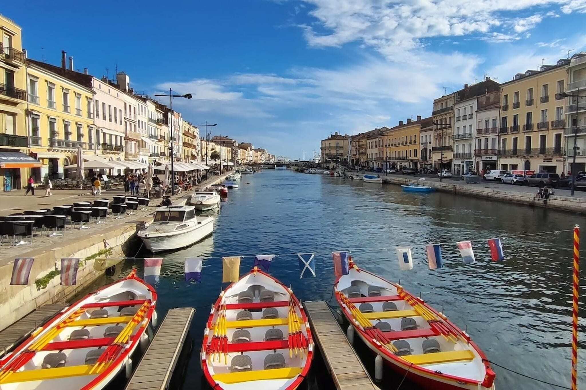 Un canale fiancheggiato da barche ormeggiate al molo, con edifici su entrambe le rive e un cielo sereno.