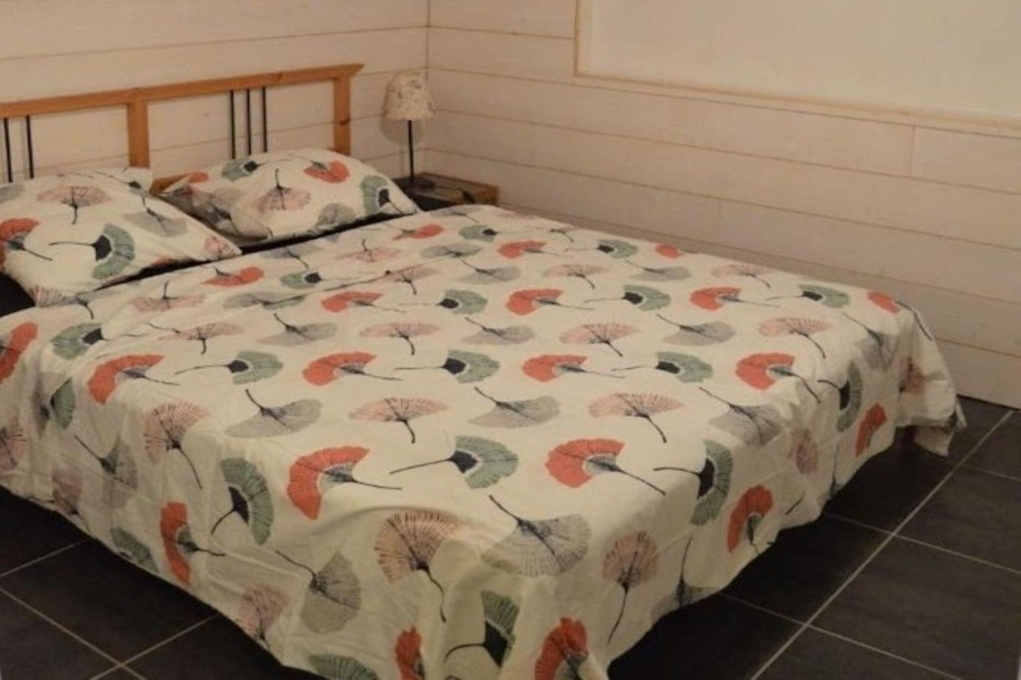 Un letto con una coperta a fiori, una testiera in legno, un comodino con una lampada e una parete spoglia.